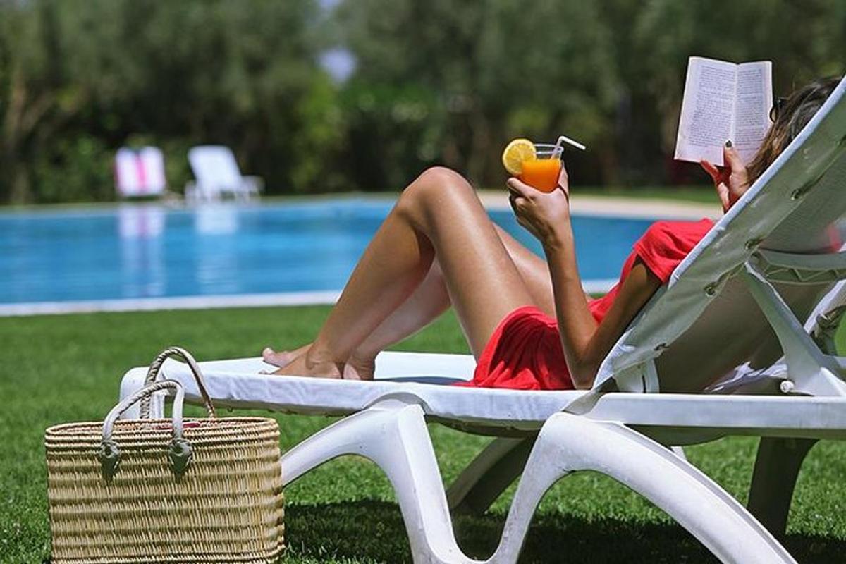 a woman sitting on a lounge chair reading a book and eating an apple