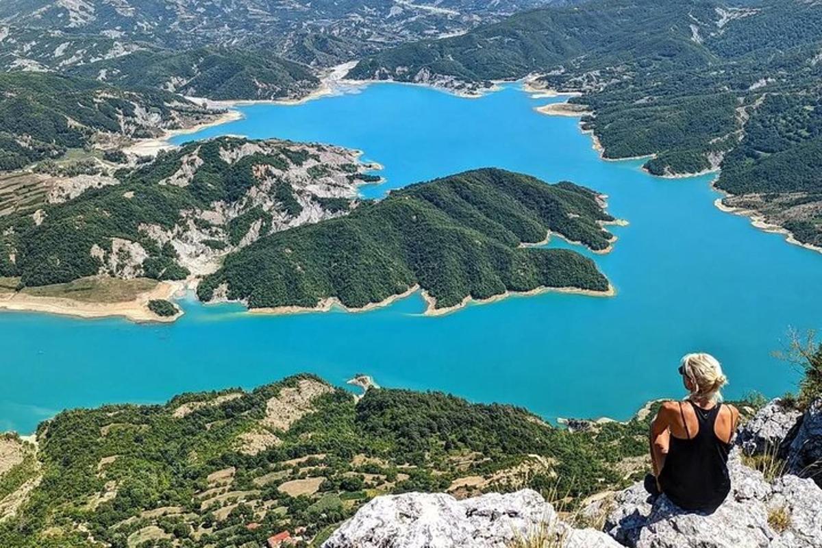 žena sedící na vrcholu hory a dívající se na jezero