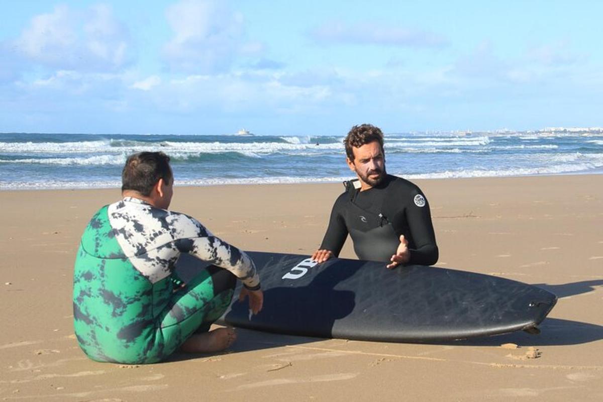 dua lelaki duduk di pantai dengan papan luncur