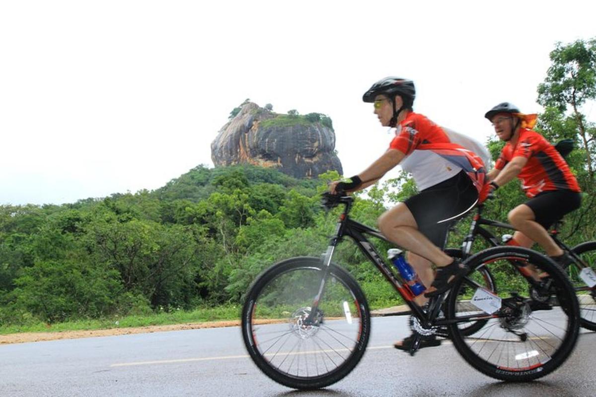 dos homes anant en bicicleta per una carretera amb una roca al fons