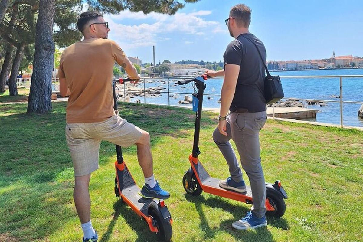 two men riding scooters on the grass near the water