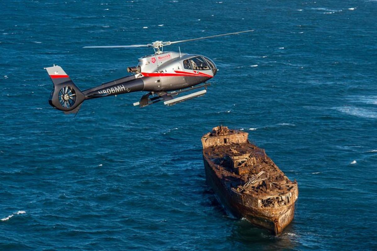 um helicóptero voando sobre o oceano com uma grande rocha