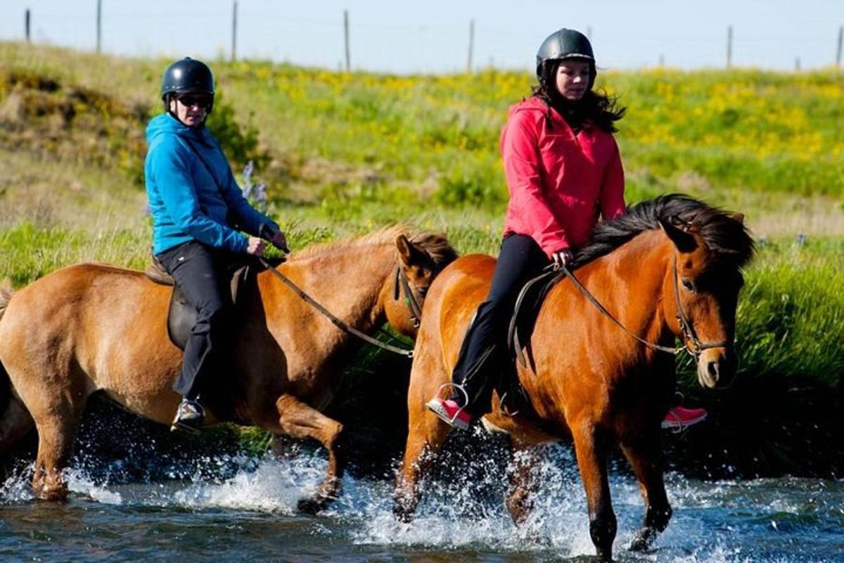 Dos personas montan a caballo por el agua.