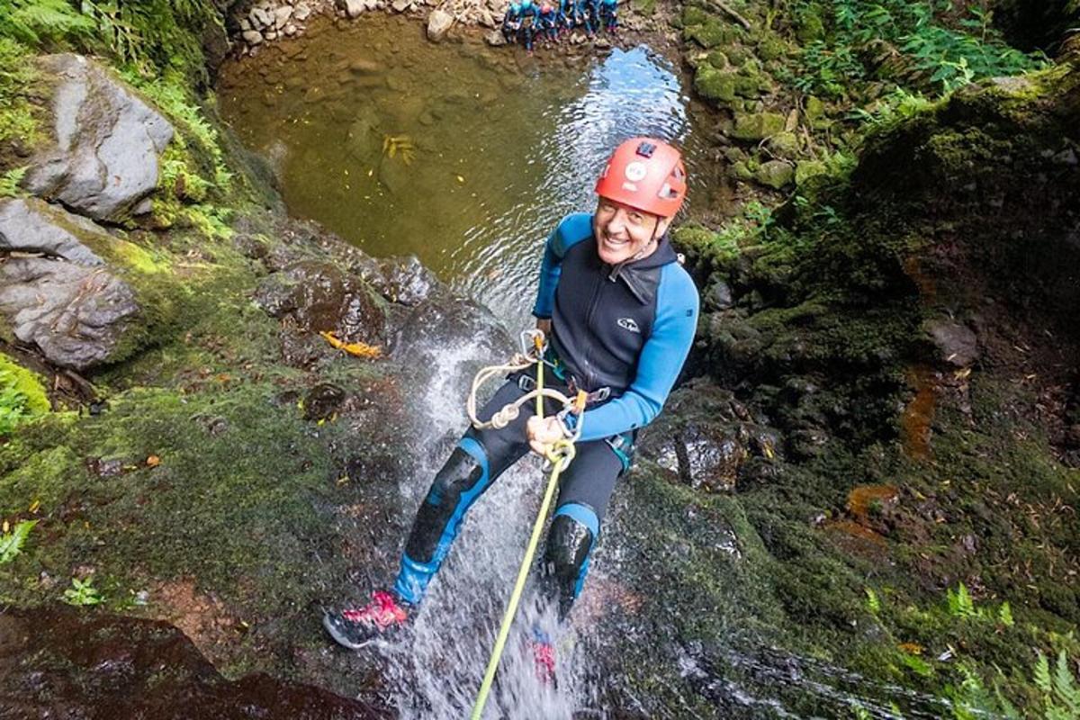 ein Mann mit Helm an einem Seil in einem Wasserfall