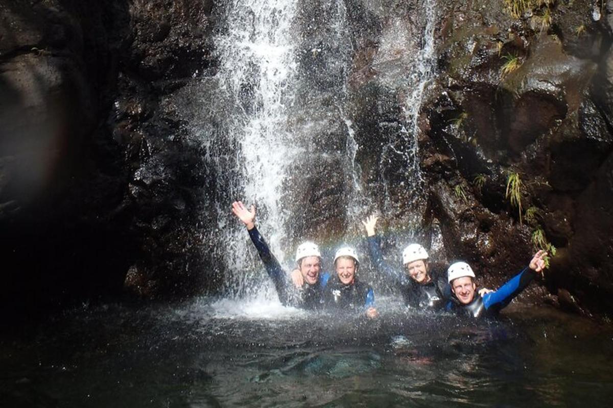 three people in the water in front of a waterfall