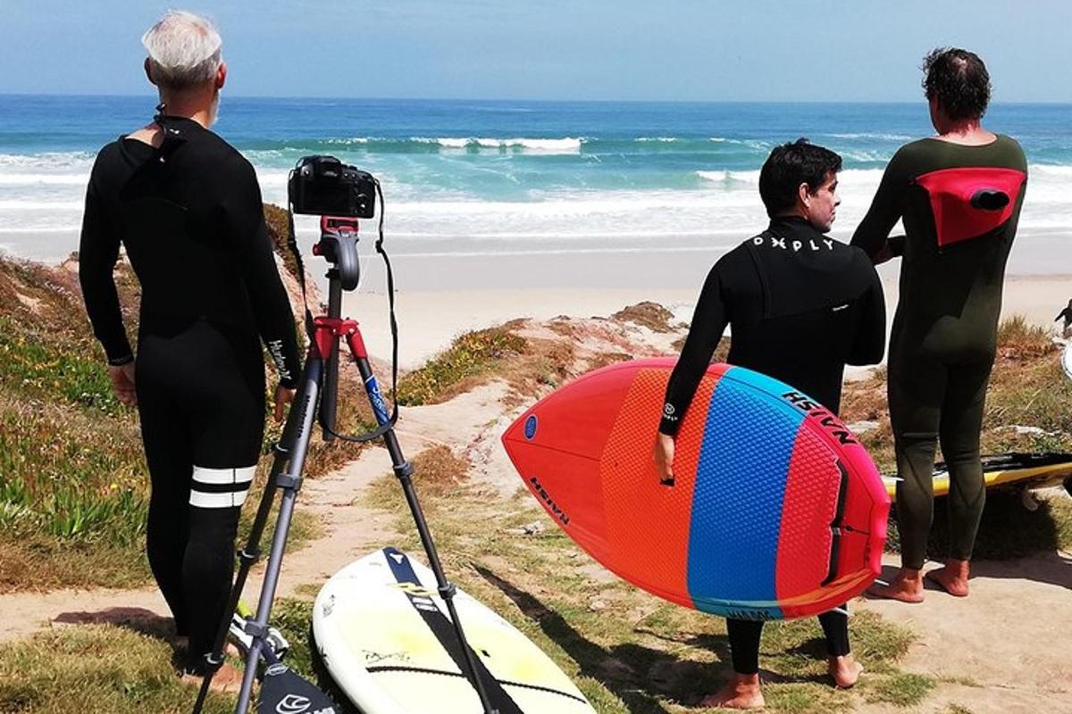 drei Männer in Neoprenanzügen stehen mit einem Surfbrett am Strand