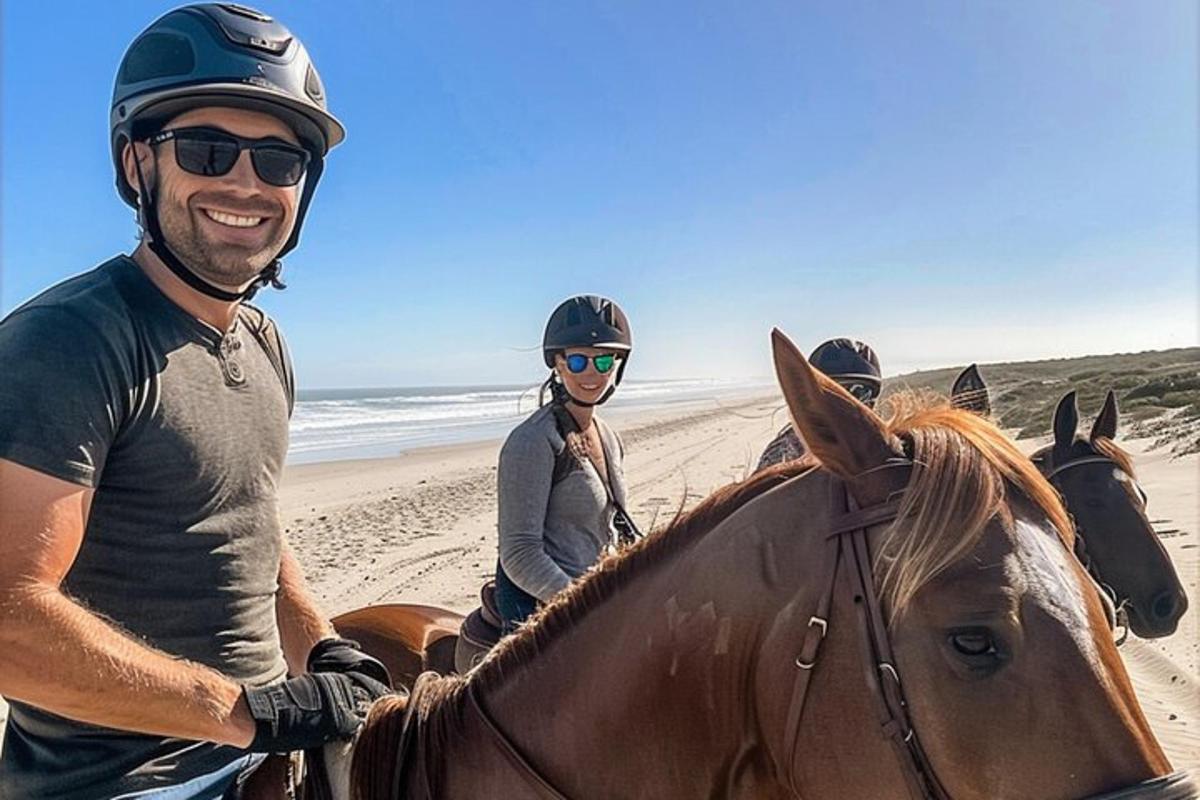 een groep mensen die op paarden op het strand rijden