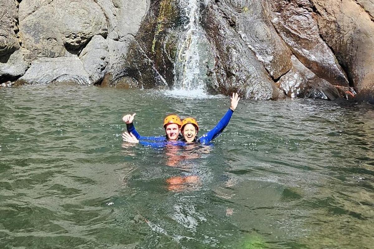 two people in the water in front of a waterfall