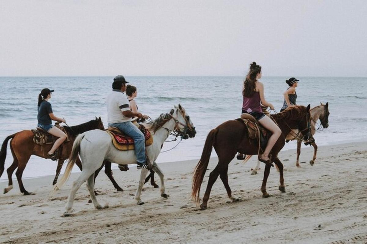 a group of people riding horses on the beach