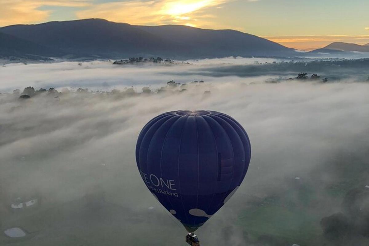 horkovzdušný balón letící nad údolím pokrytým mlhou