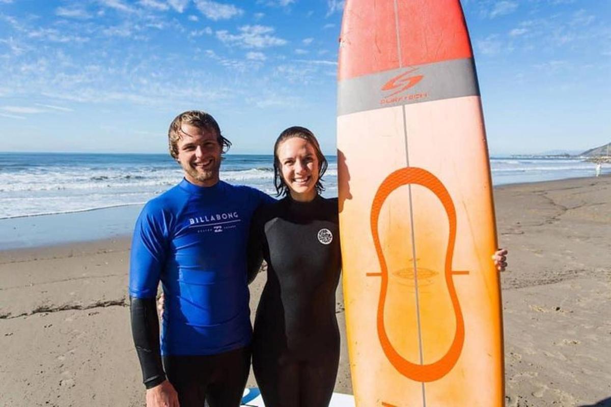 a man and woman standing on the beach with a surfboard