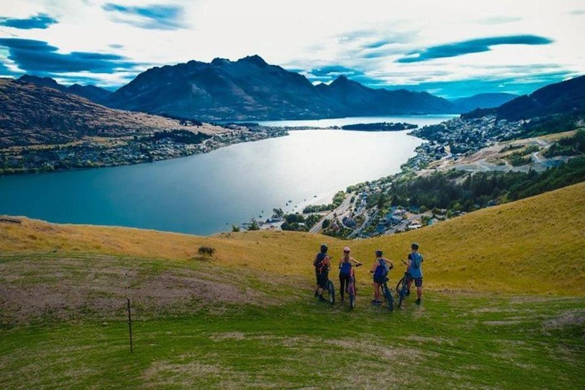 trije ljudje vozijo kolesa na hribu s pogledom na jezero