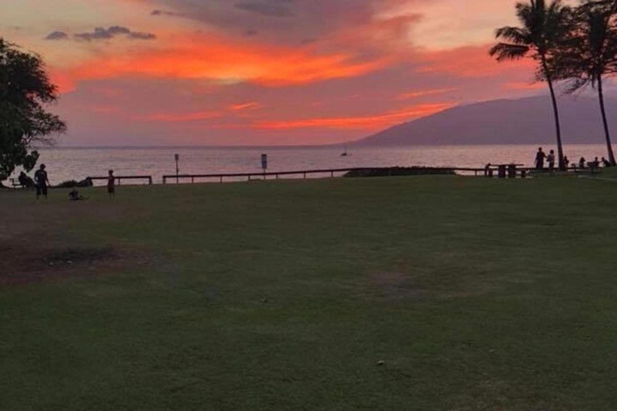 matahari terbenam di atas laut dengan orang-orang berjalan di pantai