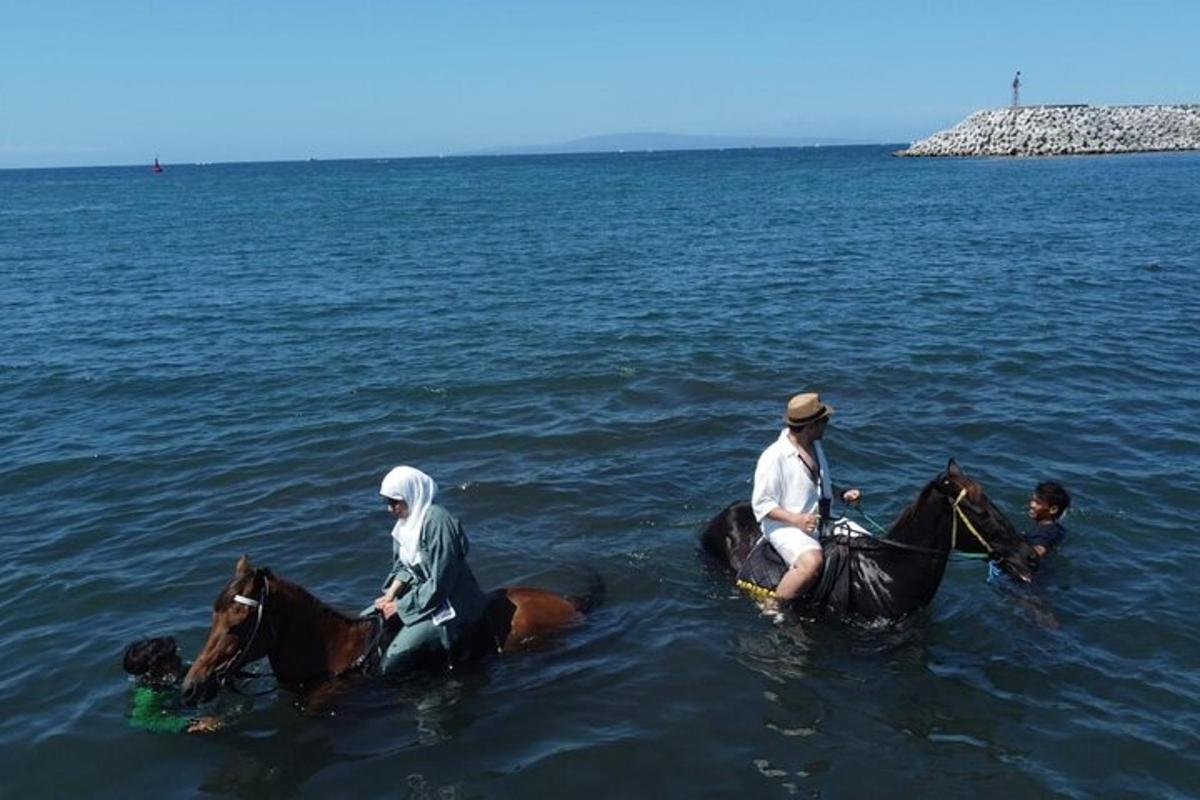 Dos hombres montando a caballo en el agua con un niño