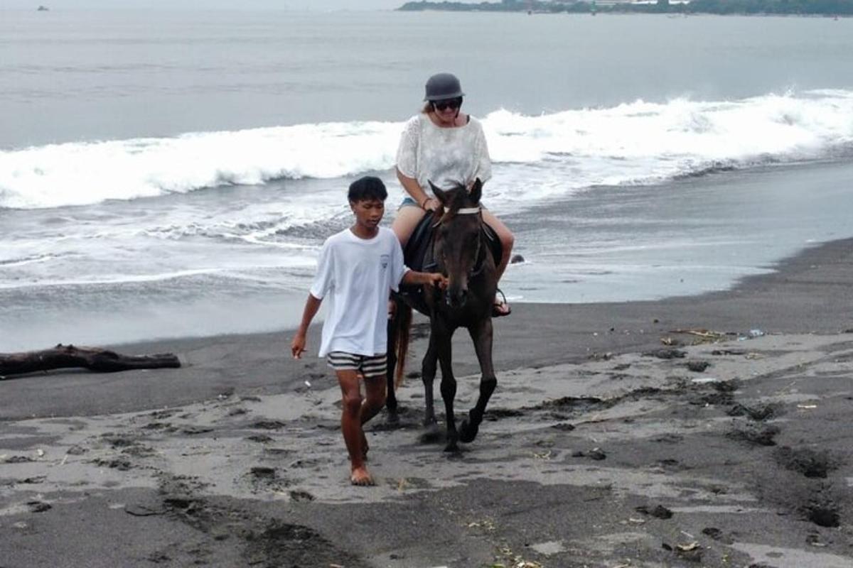 Una mujer montando a caballo en la playa con un niño.