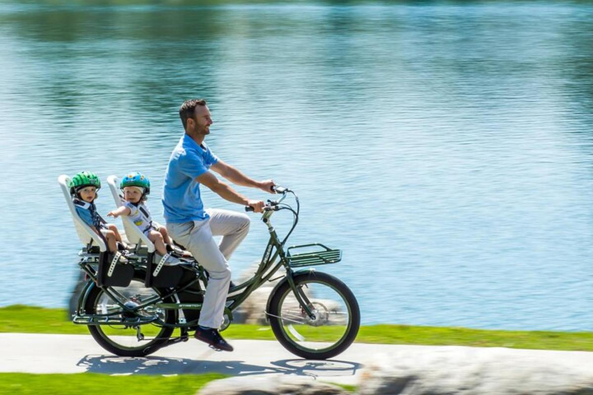 moški in dva otroka se vozita s kolesom ob vodi