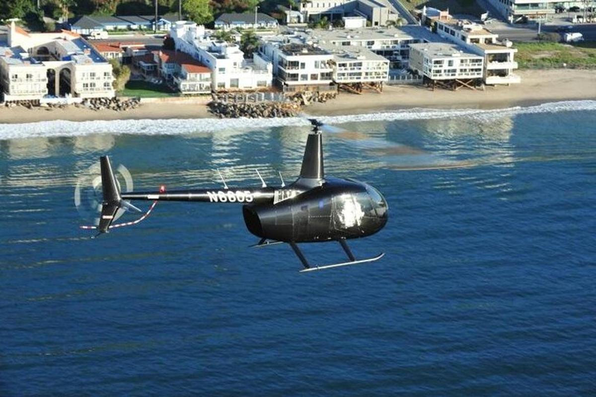 un hélicoptère noir survolant l'eau près d'une plage