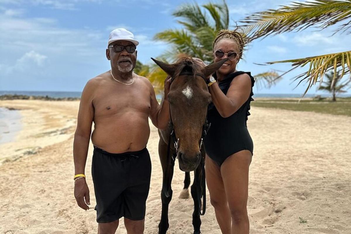 un uomo e una donna in piedi accanto a un cavallo sulla spiaggia