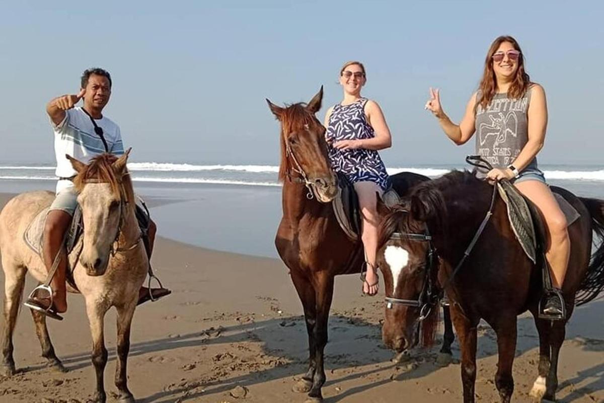 tres persones muntant a cavall a la platja
