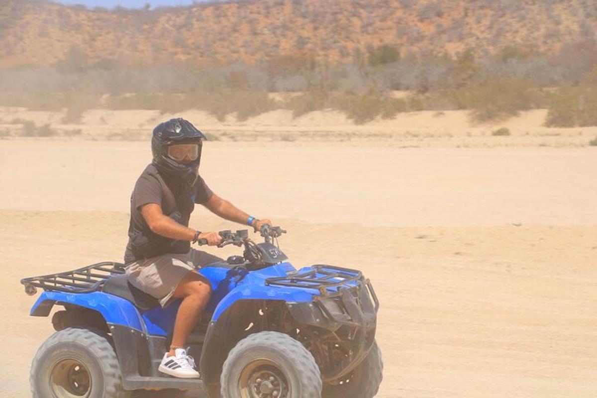 Un hombre conduciendo un vehículo todo terreno azul en el desierto.