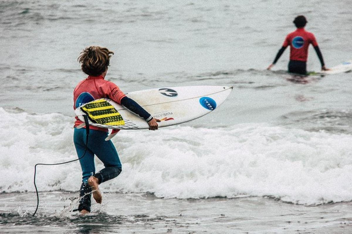 duas pessoas caminhando em direção ao oceano com uma prancha de surfe
