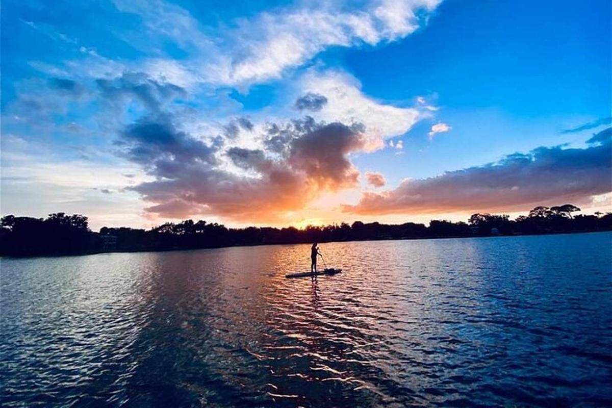 seseorang di atas papan dayung di tasik pada waktu matahari terbenam