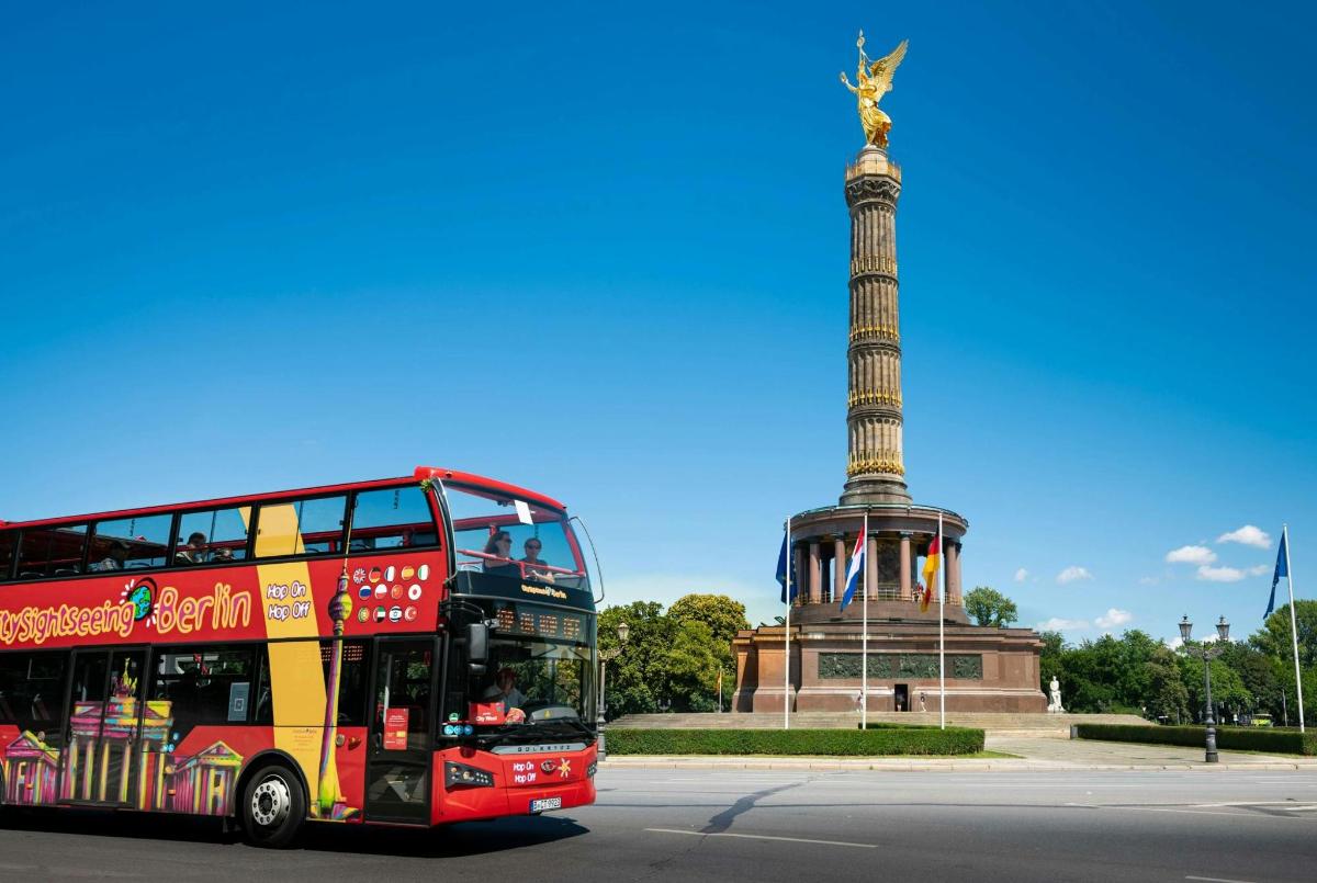 a red double decker bus driving past a statue