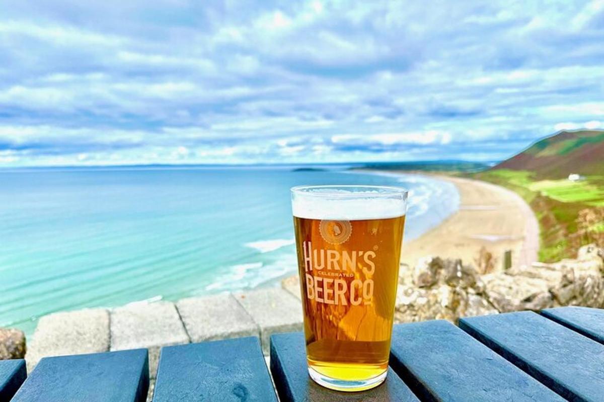 a glass of beer sitting on a picnic table near the beach