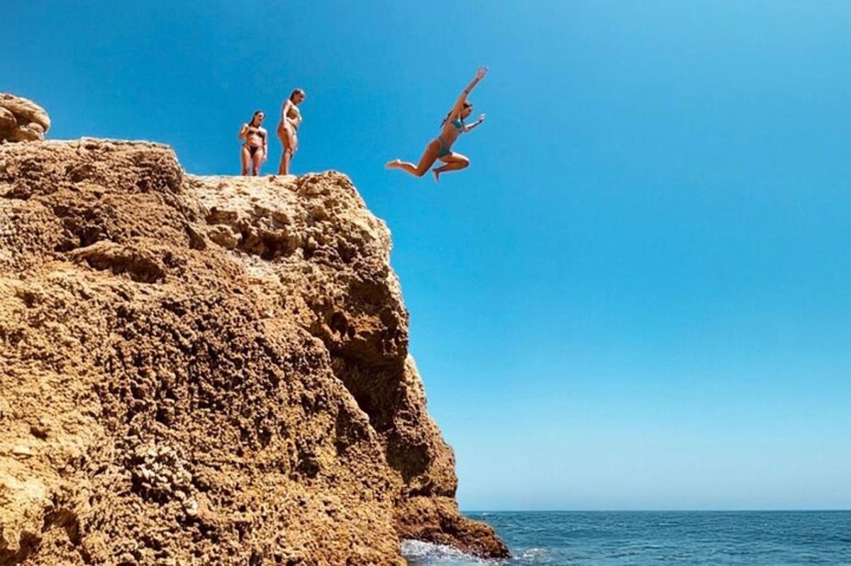a group of people jumping off a cliff into the ocean