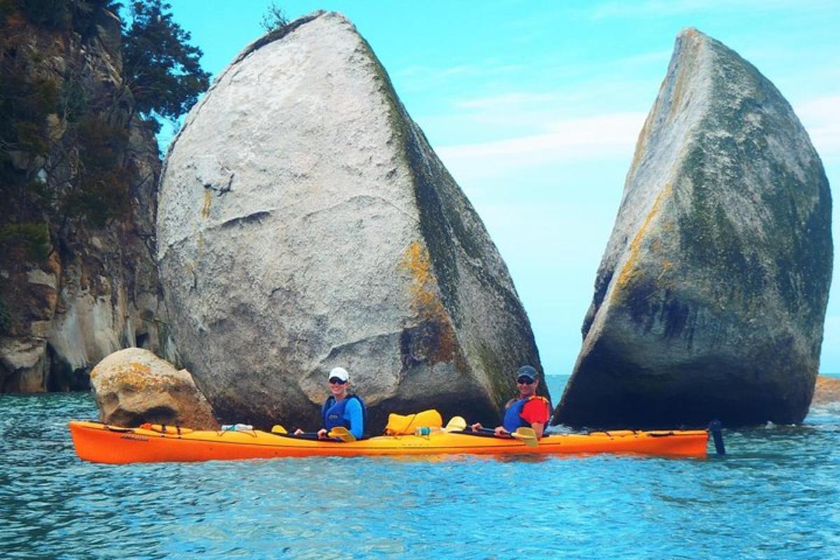 two people in a kayak in the water near two large rocks