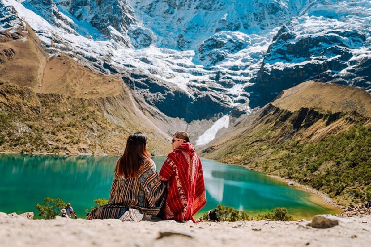 two people sitting on the beach near a mountain lake
