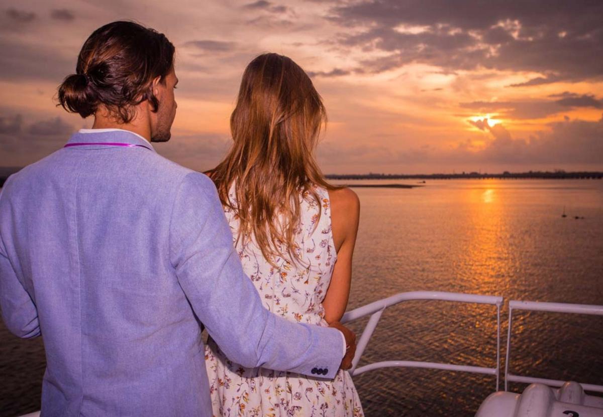 a man and woman standing on a boat looking at the sunset