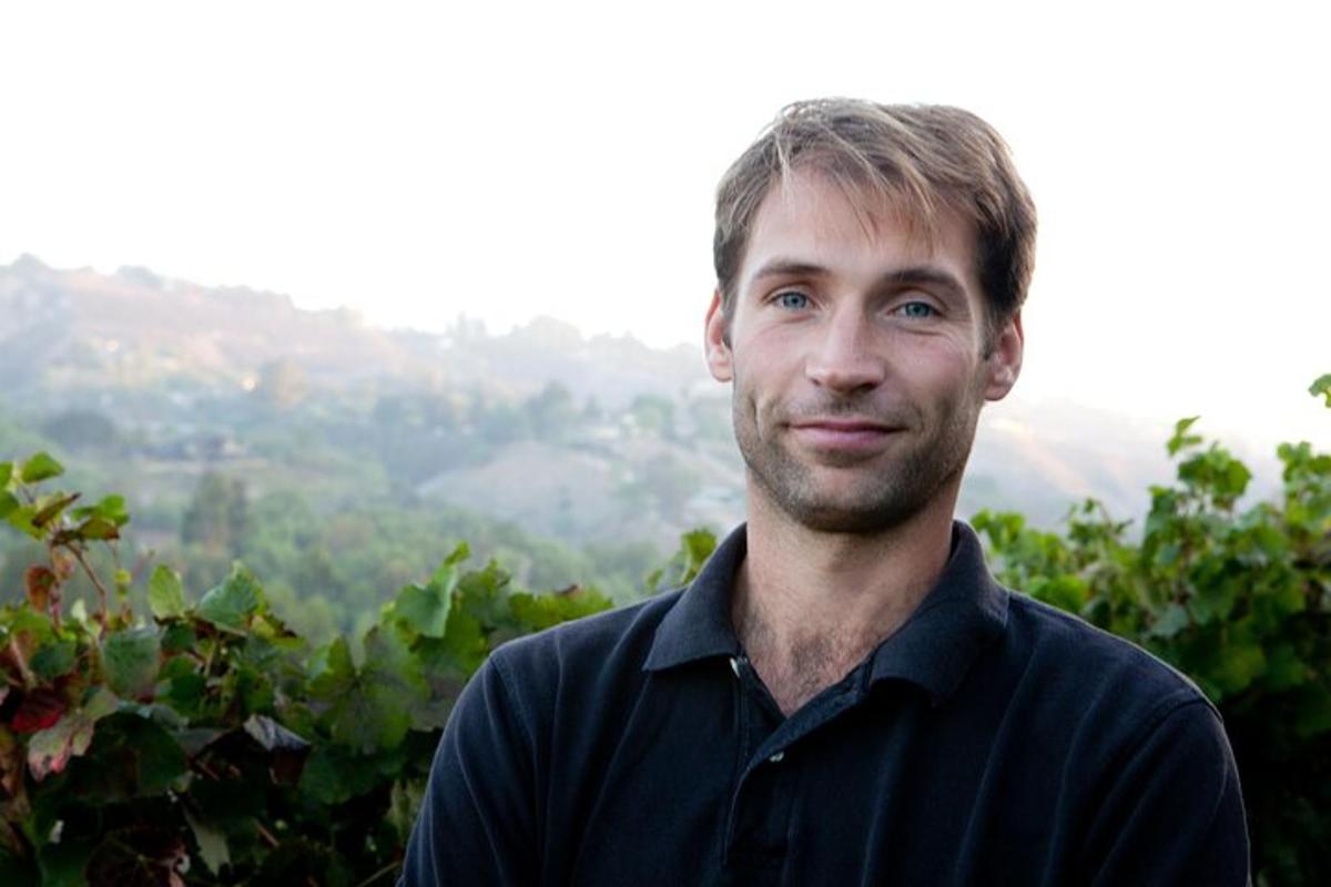 a man in a black shirt standing in a vineyard
