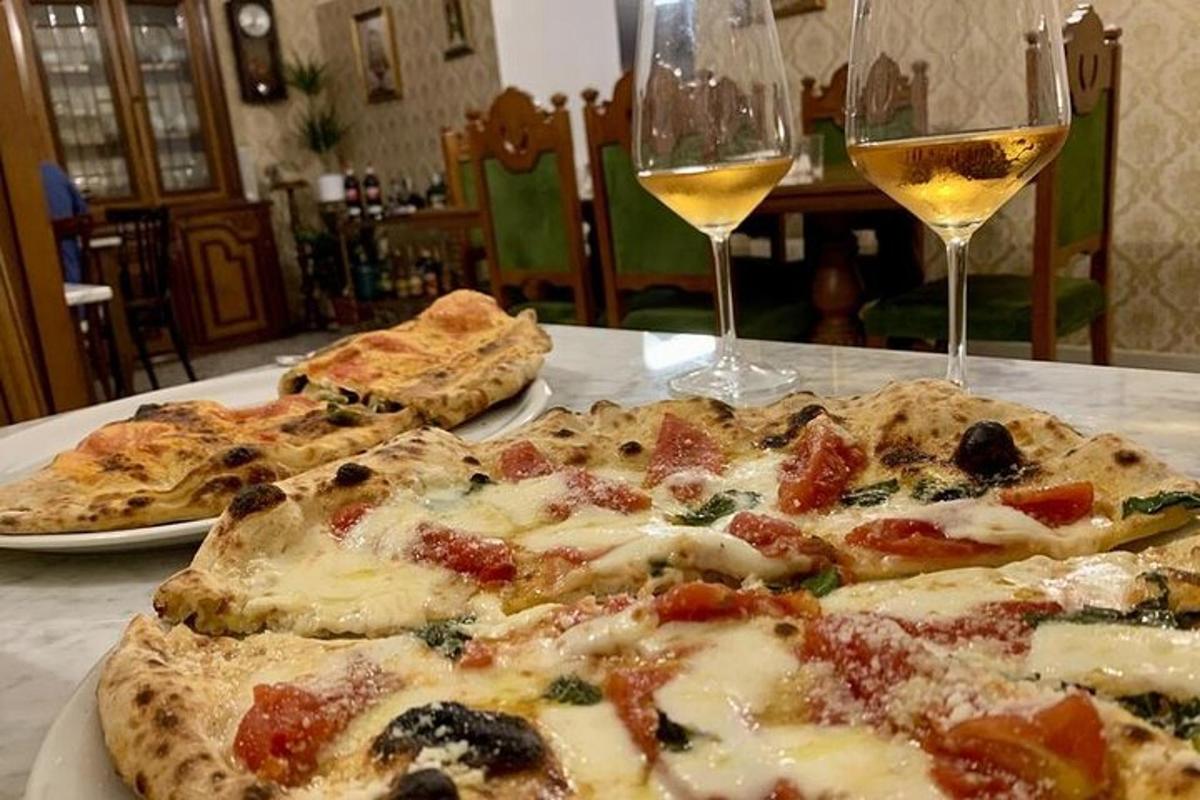 tři pizzy sedící na stole se sklenicemi vína