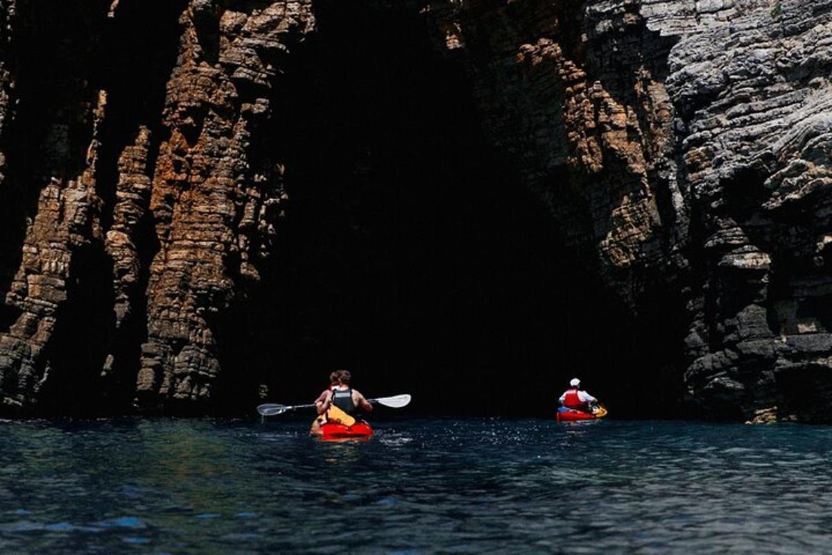 duas pessoas em caiaques na água perto de uma caverna