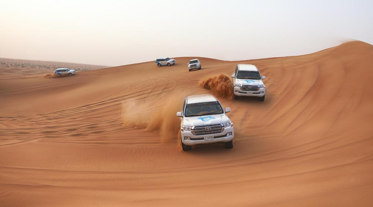 três caminhões dirigindo em uma duna de areia no deserto