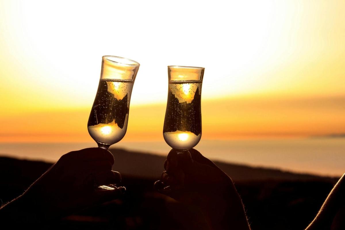 duas pessoas segurando taças de vinho em frente ao pôr do sol