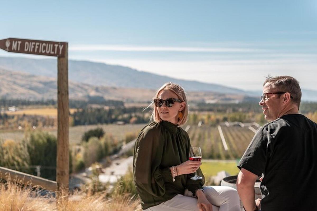 a man and a woman sitting on a hill with a glass of wine