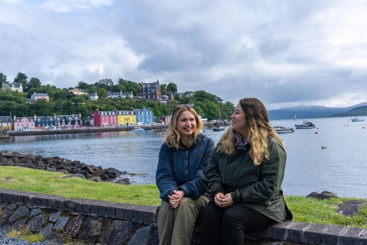 to kvinner som sitter på en steinmur ved vannet
