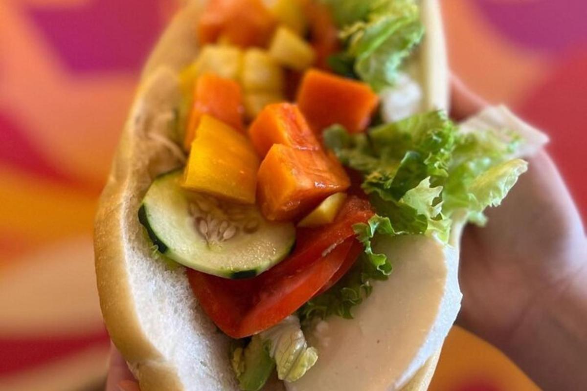 a person holding a sandwich with vegetables and lettuce