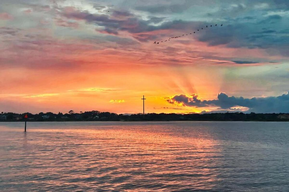 a sunset over a body of water with a flock of birds