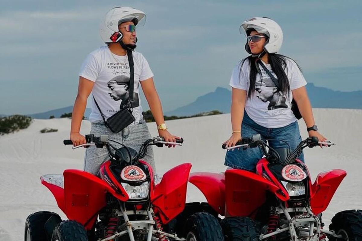 two people standing on four wheelers in the sand