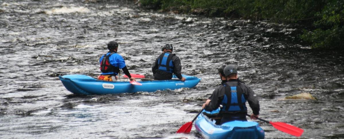 tři lidé jsou v kajacích na řece