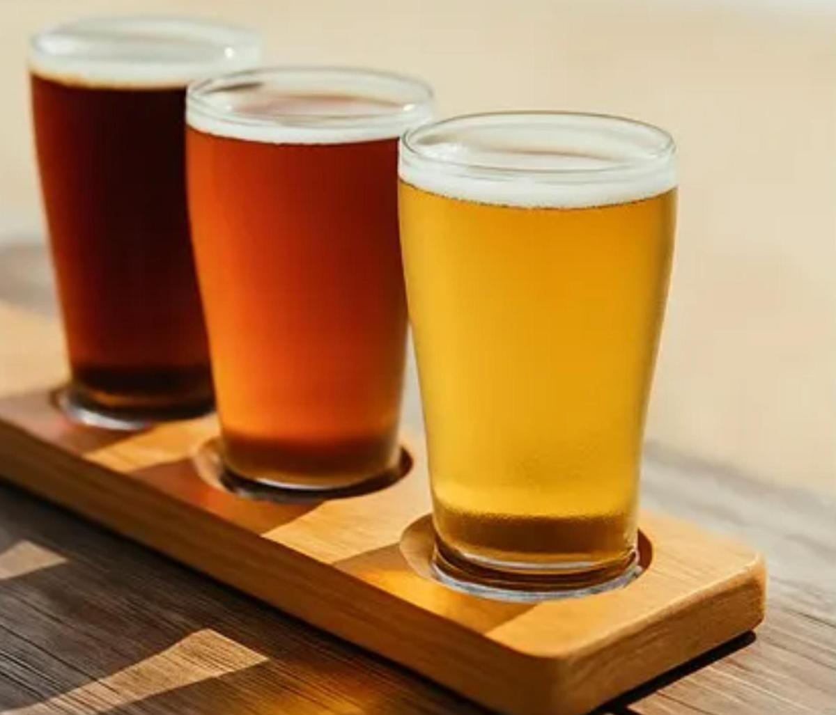 four glasses of beer sitting on a wooden tray