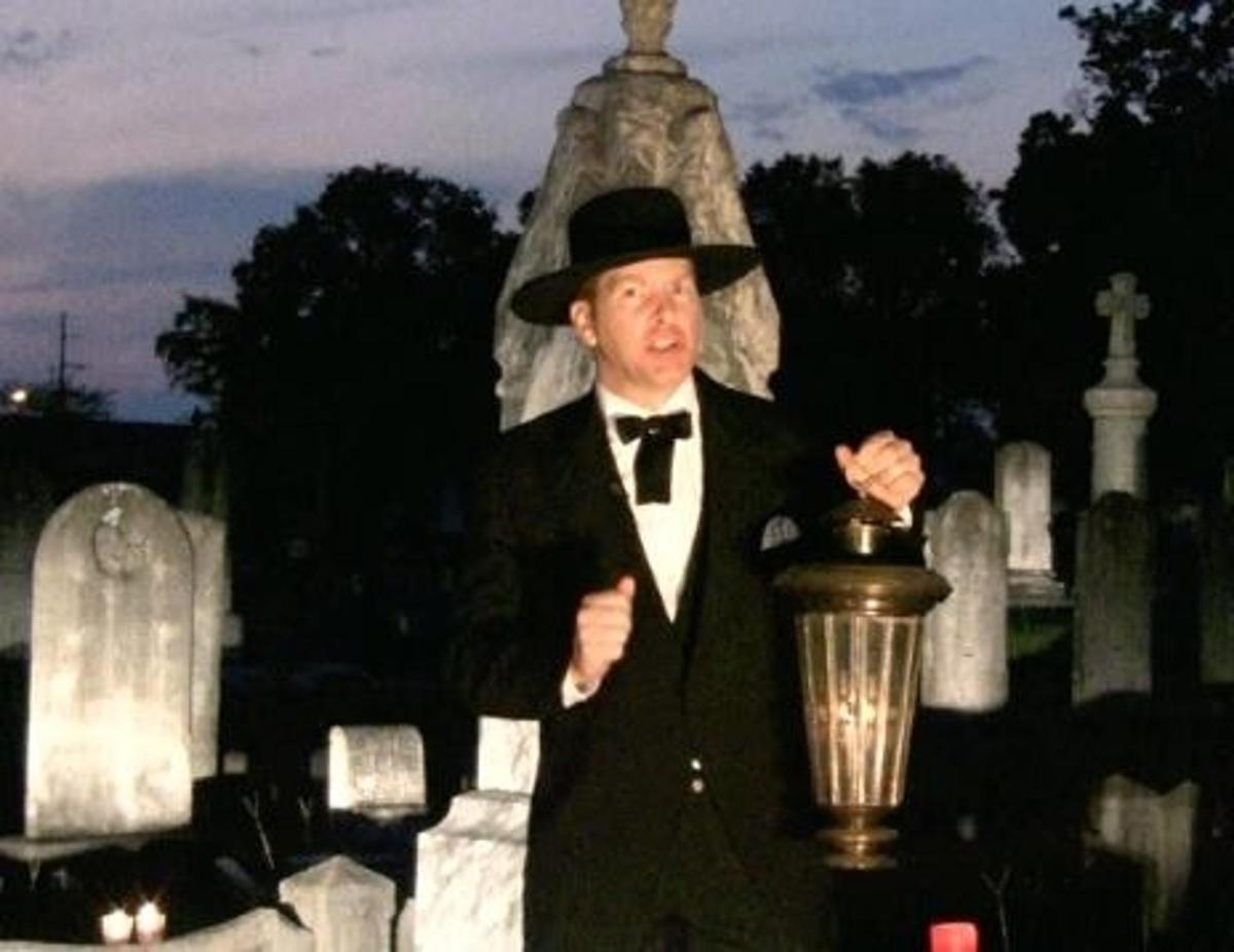 a man in a suit and hat standing in front of a cemetery