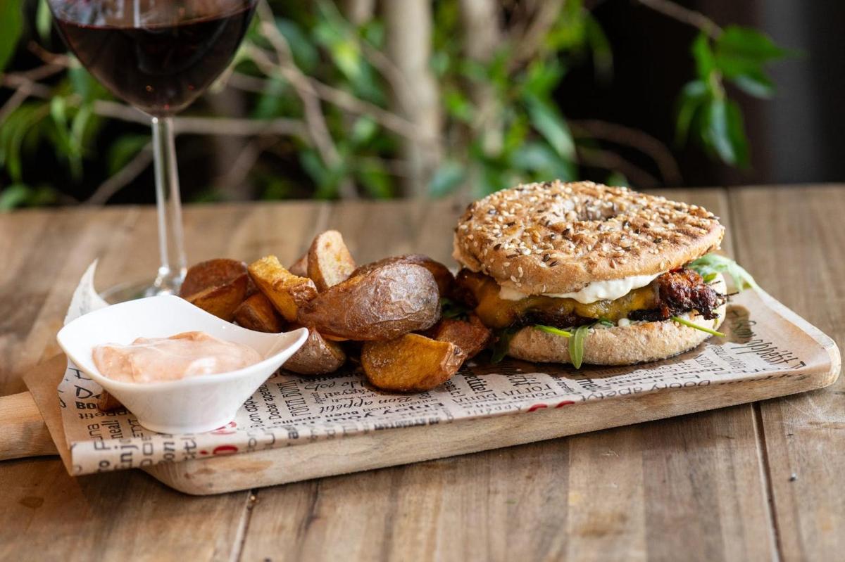 a sandwich and potatoes on a wooden table with a glass of wine