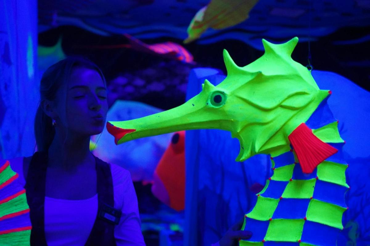 a woman standing next to a green dinosaur toy