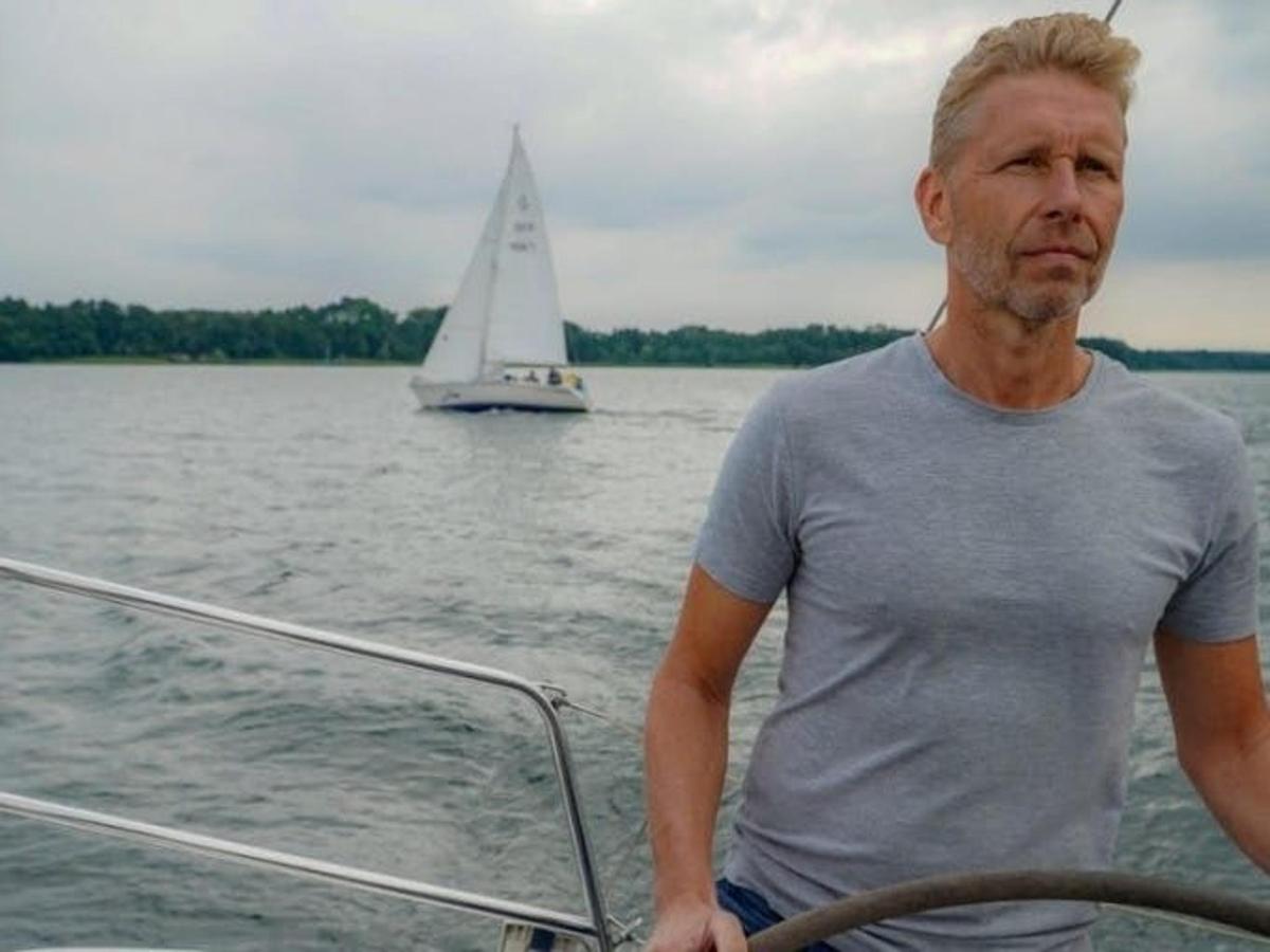 a man standing on the front of a boat with a sailboat