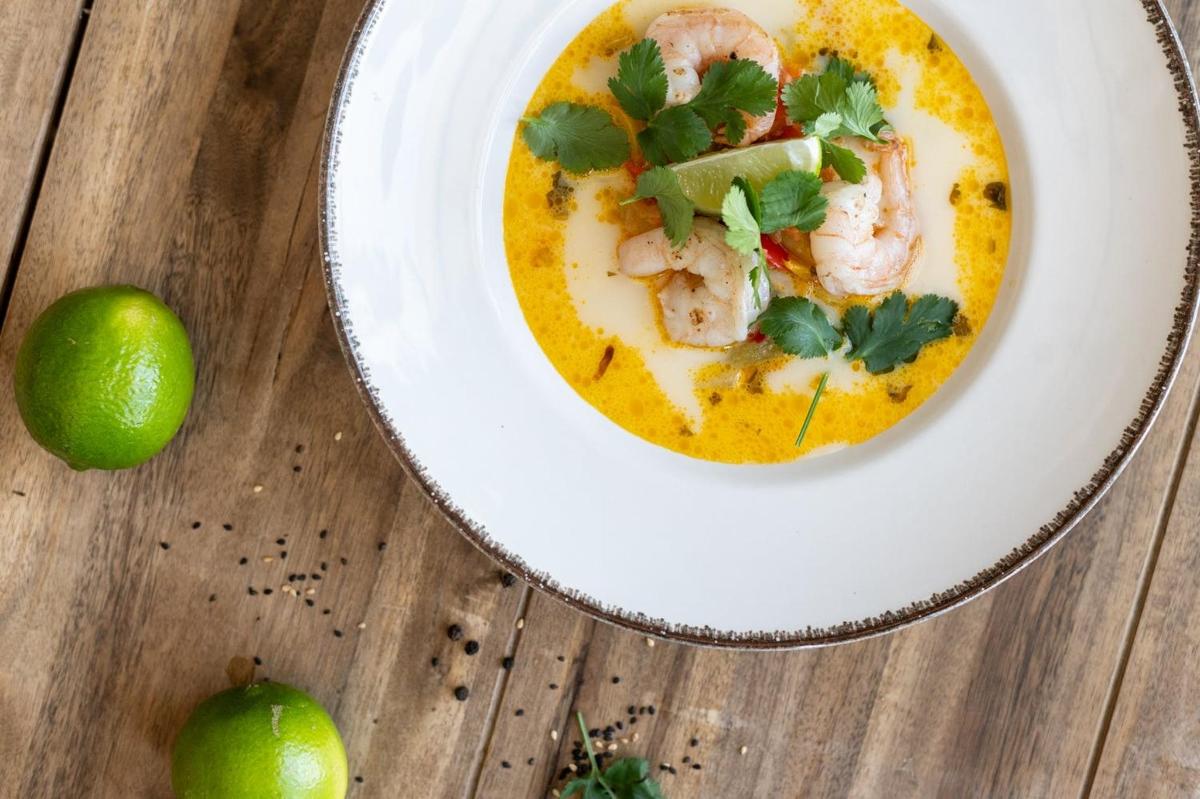 a plate of shrimp soup with a lime on a wooden table