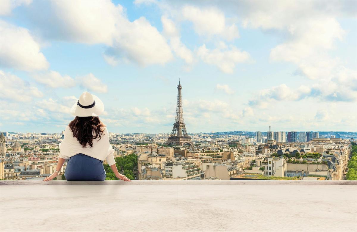a woman sitting on a ledge looking at the eiffel tower